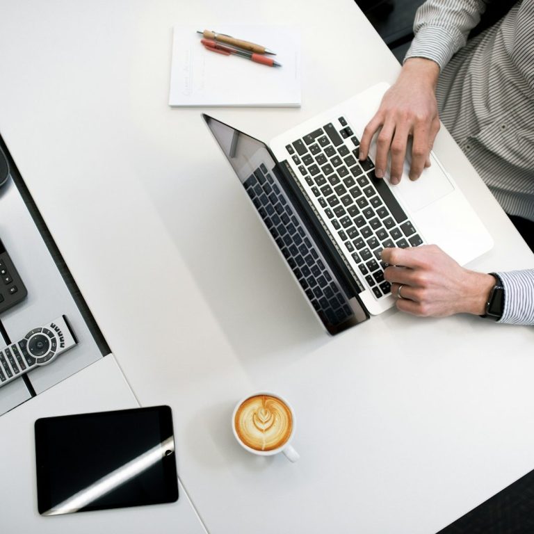 Professionelle Texte schreiben lassen: KI alt aussehen lassen! Eine Person tippt auf einem Laptop, daneben eine Tasse Kaffee und ein Tablet. Zu sehen ist, wie ein Mensch Texte erstellt.